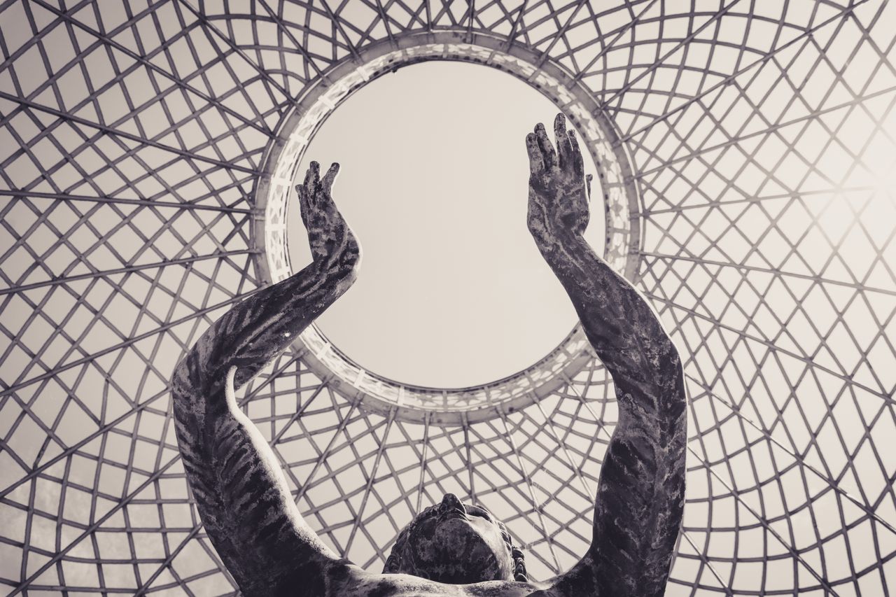 Dramatic sculpture reaching towards a circular sky framed by intricate lattice structure.